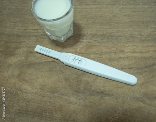 Positive pregnancy test and glass of milk on wooden background photo