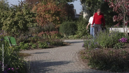 Senior couple with German Pinscher dog walking through a well gardened park with well trimmed bushes and beautiful flowers. photo