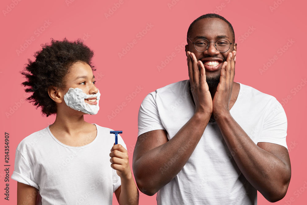 Satisfied African American male touches cheeks, glad to have soft skin  after shaving. Happy dark skinned