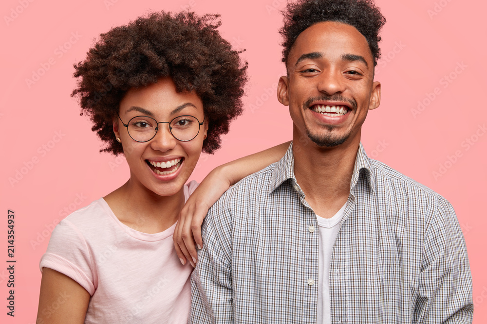 Portrait of happy smiling African American couple feel glad to meet with friends, share news with each other, look joyfully at camera. Lovely female has Afro hairstyle leans at shoulder of companion Portrait of happy smiling African American couple feel glad to meet with friends, share news with each other, look joyfully at camera. Lovely female has Afro hairstyle leans at shoulder of companion