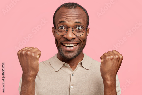 Fotografia Wow, I achieved it! Happy black male with joyful expression, presses hands in fi