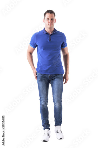 Cool relaxed young adult man in polo shirt and jeans walking and looking at camera. Full body isolated on white background. 