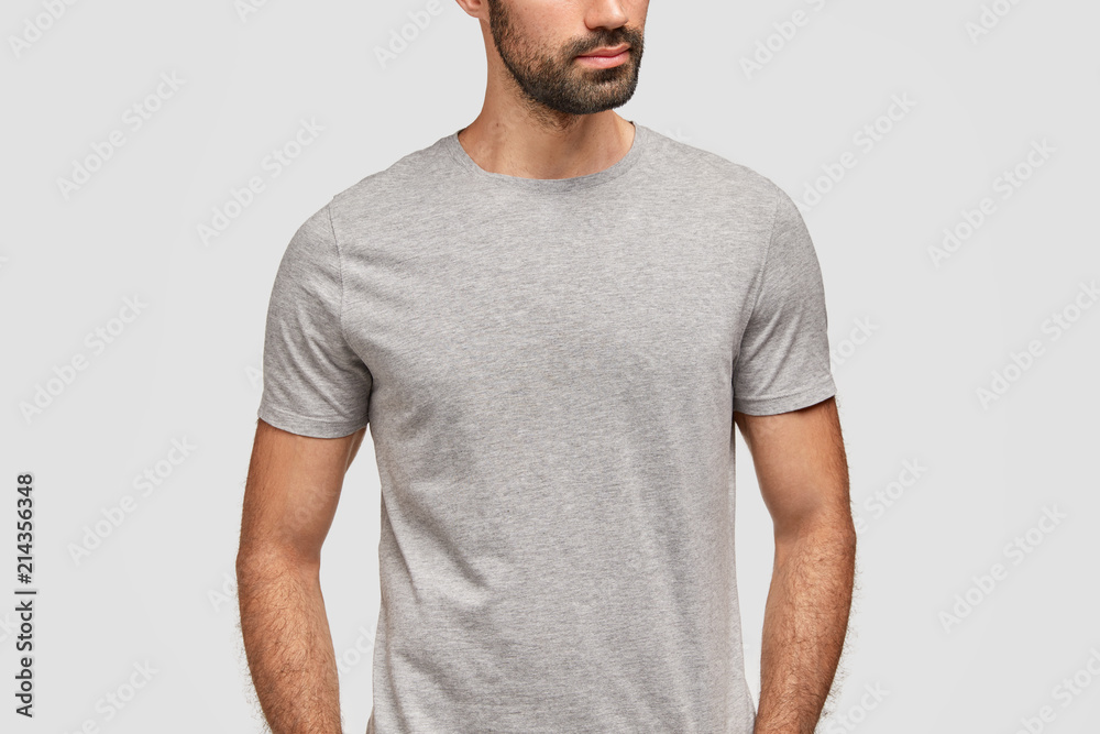 Cropped view of unrecongnizable bearded male dressed in casual grey t shirt with copy space for your designing content or logo, stands alone against white background, has strong muscular body Cropped view of unrecongnizable bearded male dressed in casual grey t shirt with copy space for your designing content or logo, stands alone against white background, has strong muscular body