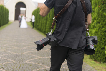 Professional wedding photographer takes pictures of the bride and groom in garden, the photographer in action with two cameras on a shoulder straps.