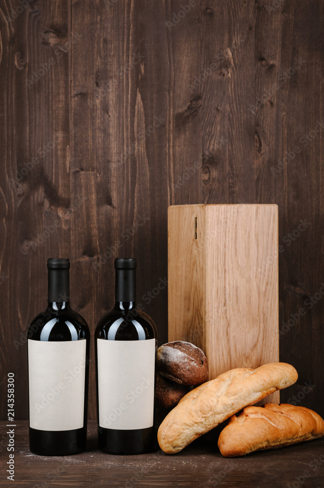 Naklejka premium wine composition with bread, two bottles in box and wineglass on wooden background