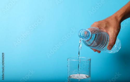 Closeup of pouring mineral water from bottle into glass by man's hand. 
