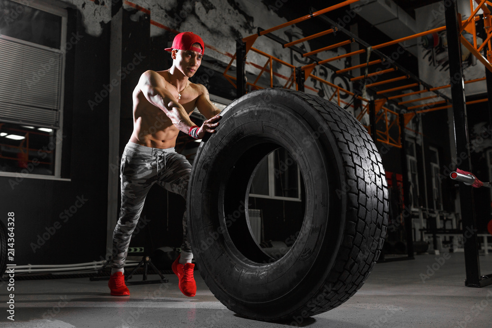 Shirtless man flipping heavy tire at gym