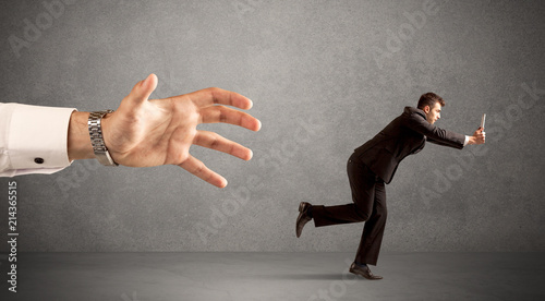 Young miniature businessman running from a big hand with light grey background