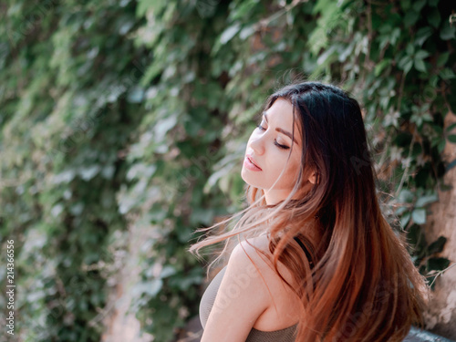 Portrait of young attractive girl with smile. Woman with oriental face, brown eyes and stylish ombre dyed long haistyle on foliage background. Street style.