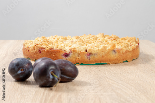 Frische reife Pflaumen vor einem fertigen Pflaumenkuchen auf einem Holztisch photo