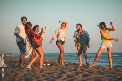 Happy friends sitting on the beach singing and playing guitar during the sunset photo