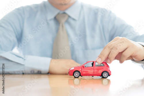 Businessman by a desk holding a toy car.
