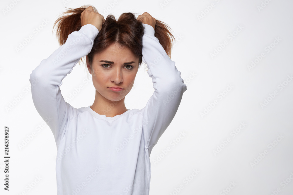 Portrait of playful funny teenage girl wearing blue shirt having fun indoors, holding hair in two tails, grimace as being unsatisfied, not getting what she wants. Human emotions and expressions concep Portrait of playful funny teenage girl wearing blue shirt having fun indoors, holding hair in two tails, grimace as being unsatisfied, not getting what she wants. Human emotions and expressions concep