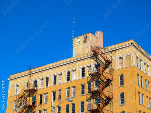 Old building facade and a emergency staircase in Greenville, TX, USA. Color view of a red brick wall with metal fire escape against clear blue sky on bright sunny day.