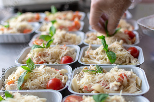 preparation of dietary dishes in the kitchen for the delivery of dietary lunch, basil, tomato cherry,  cheese, pasta and chicken fillet. concept of takeaway food. selective focus