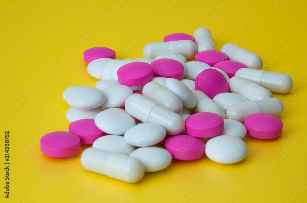 A pile of pills of white and pink on a yellow background.