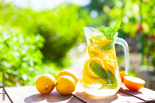 Summer fresh cold drink beverages. Ice Lemonade in the jug and lemons and orange with mint on table