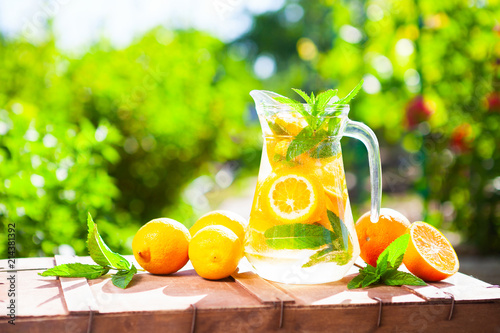 Summer fresh cold drink beverages. Ice Lemonade in the jug and lemons and orange with mint on table