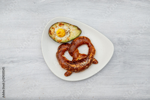 Eggs baked in avocado on plate with pretzel