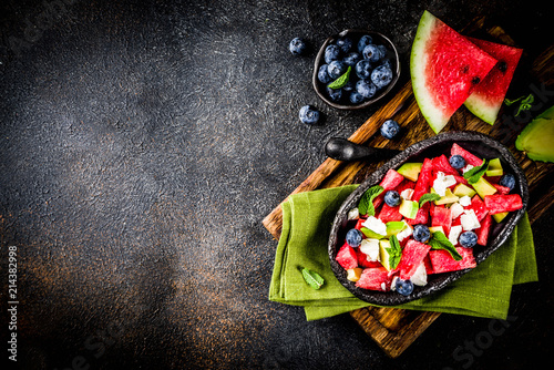 Summer food concept, fresh cold watermelon salad with feta cheese, blueberry, avocado and mint, dark rusty background copy space