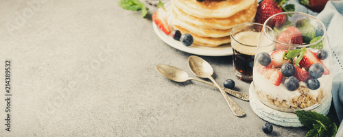 Healthy breakfast with oatmeal granola with berries and yogurt and panccakes on light gray concrete background. Healthy food concept with copy space. Banner. Retro style toned.