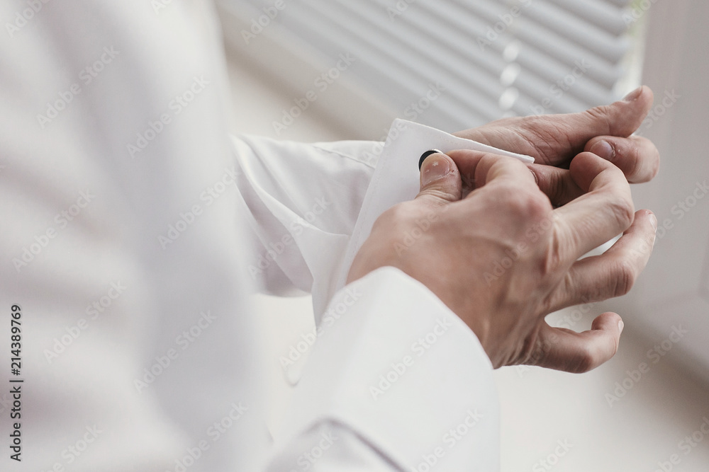 Groom getting ready in the morning in the room. man hands holding cufflinks, standing at window light in hotel. preparation for wedding day Groom getting ready in the morning in the room. man hands holding cufflinks, standing at window light in hotel. preparation for wedding day