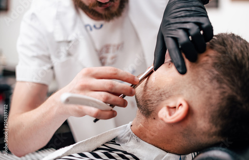 Shave beards in barbercos. Men's haircut and facial care. Barber makes a haircut to the client.