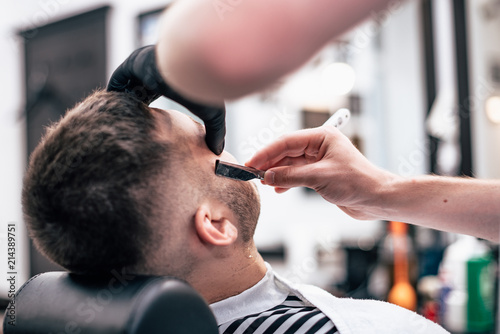 Shave beards in barbercos. Men's haircut and facial care. Barber makes a haircut to the client.