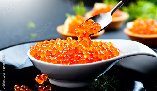 Caviar in a spoon. Salmon caviar in a bowl over black background. Closeup trout caviar
