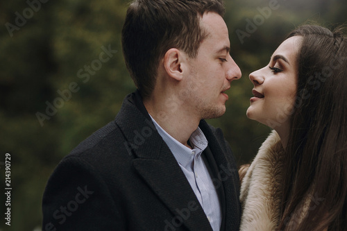 gorgeous wedding couple hugging in winter snowy park. stylish bride in coat and  groom embracing under  trees in winter forest. romantic sensual moment of newlyweds © sonyachny