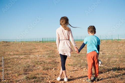 small brother and sister refugees holding hands standing among desert on state border