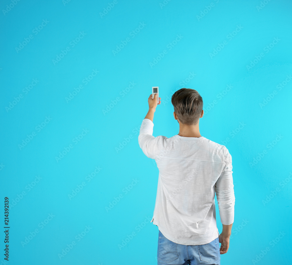 Young man with air conditioner remote on color background
