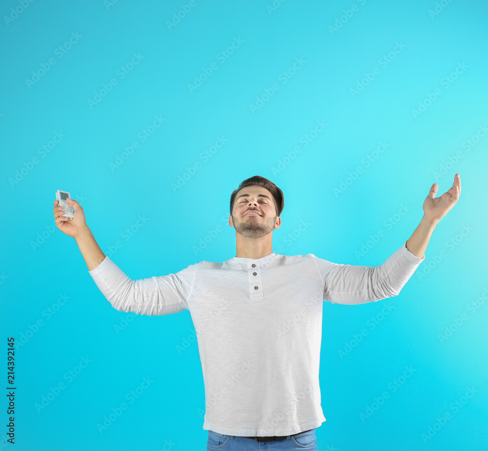 Happy young man with air conditioner remote on color background Happy young man with air conditioner remote on color background