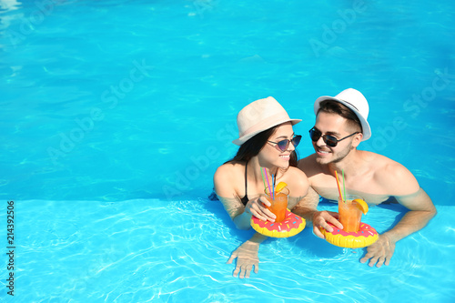 Young couple with refreshing cocktails in swimming pool on sunny day