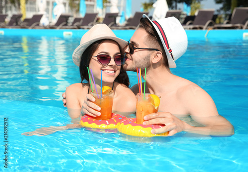 Young couple with refreshing cocktails in swimming pool on sunny day