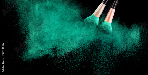 Cosmetics brush and explosion colorful makeup powder on black photo