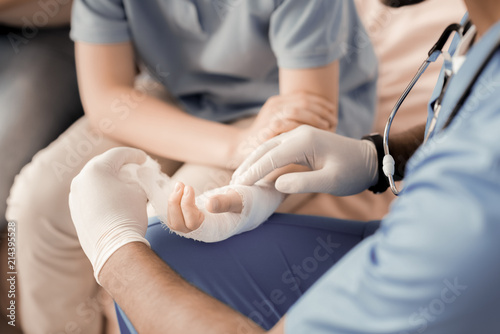 Treat me. Professional medical worker having special instrument and wearing sterile gloves while dressing injured hand of his patient