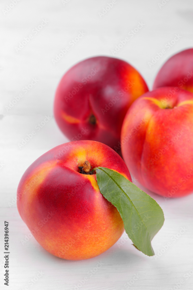 Ripe large nectarines with a green leaf close-up on a white wooden background Ripe large nectarines with a green leaf close-up on a white wooden background