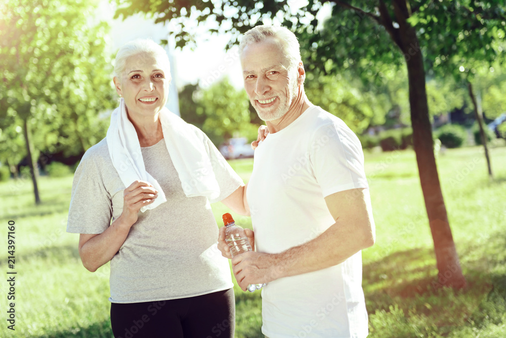 Happy together. Positive smiling aged couple looking glad while walking in a park together