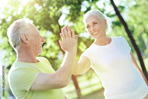 Giving five. Happy cheerful positive aged man giving five to his kind smiling wife while being outside