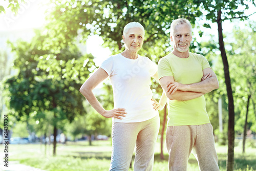 Aged couple. Pleasant positive aged couple standing together in a beautiful park
