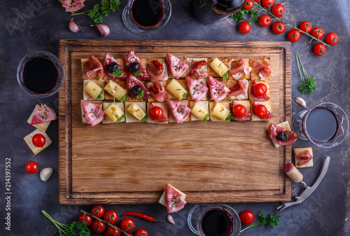 Wooden board with pinxtos or tapas with jamon, ham and sausage, flat lay