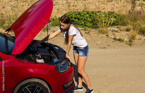 A broken car on the road, the girl checks the oil level