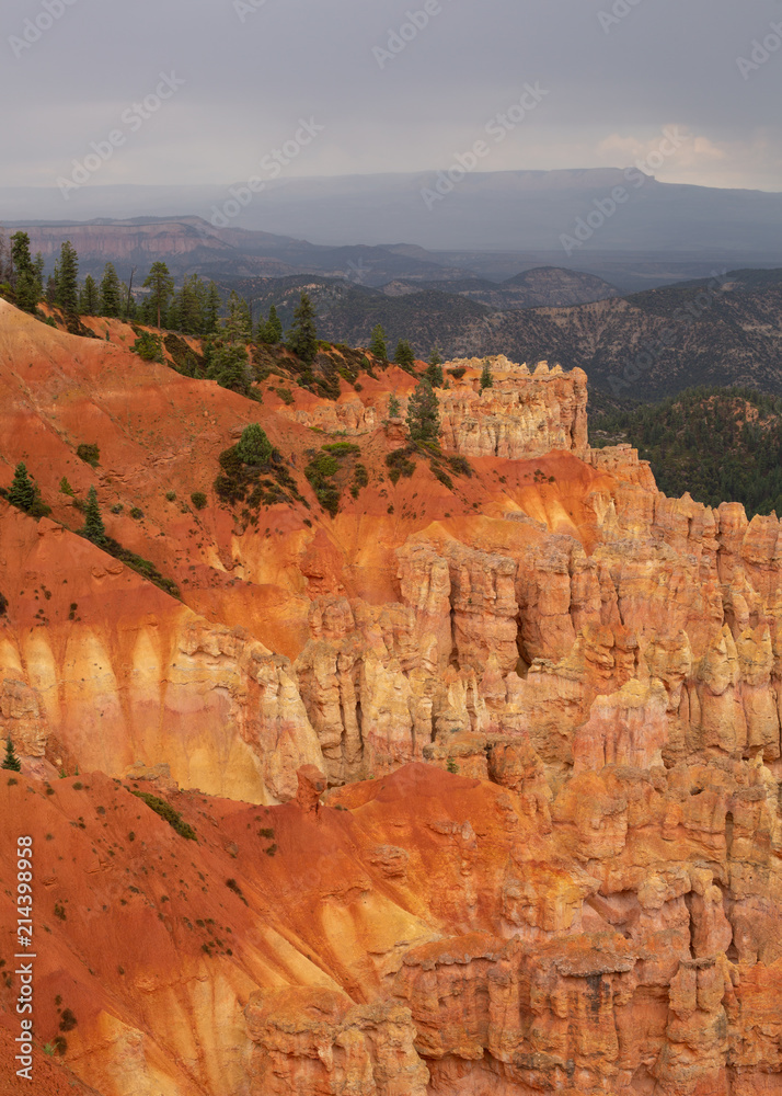 Orange and yellow cliffs topped with green pines under a cloudy sky in Bryce Canyon national park