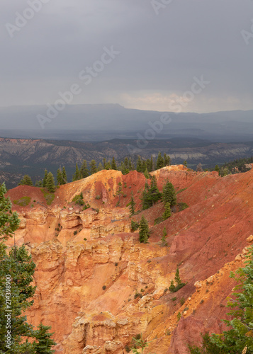 Eroding cliffs of orange and yellow topped with green pines under a softly raining cloudy sky in Bryce Canyon national park