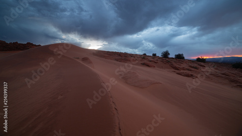 Wind blows red sand over the curving line of a dune in Southern Utah