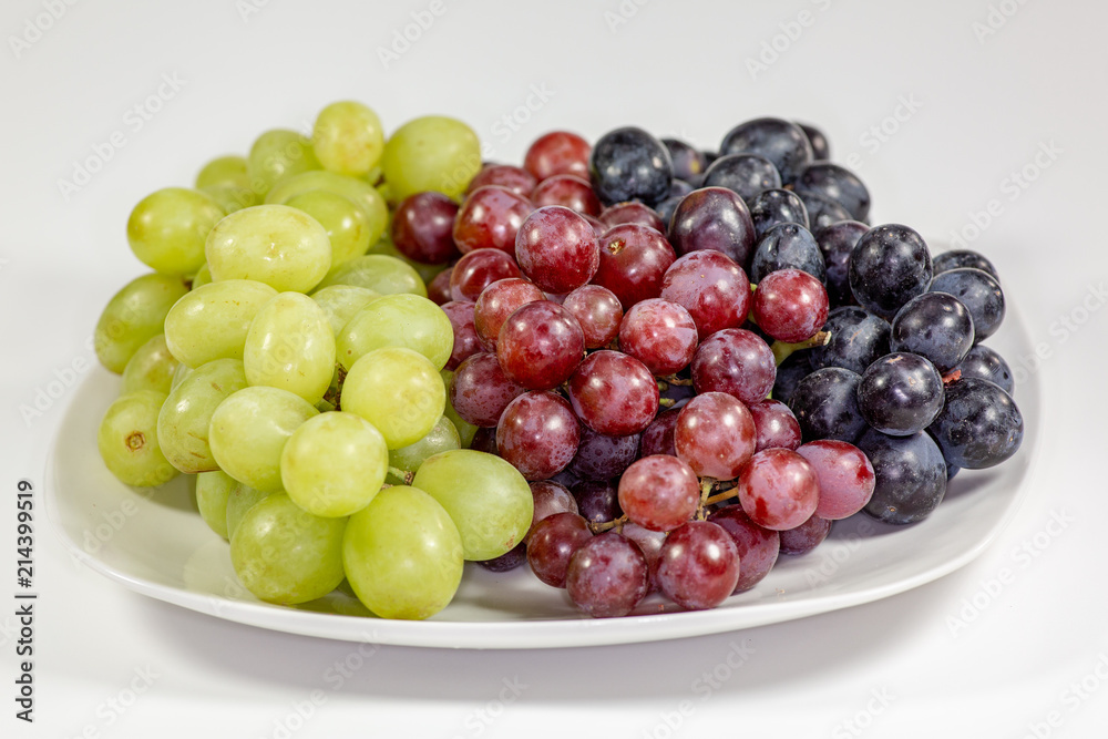 Black, red, green seedless grapes in a deep white bowl on a white tale waiting to be eaten