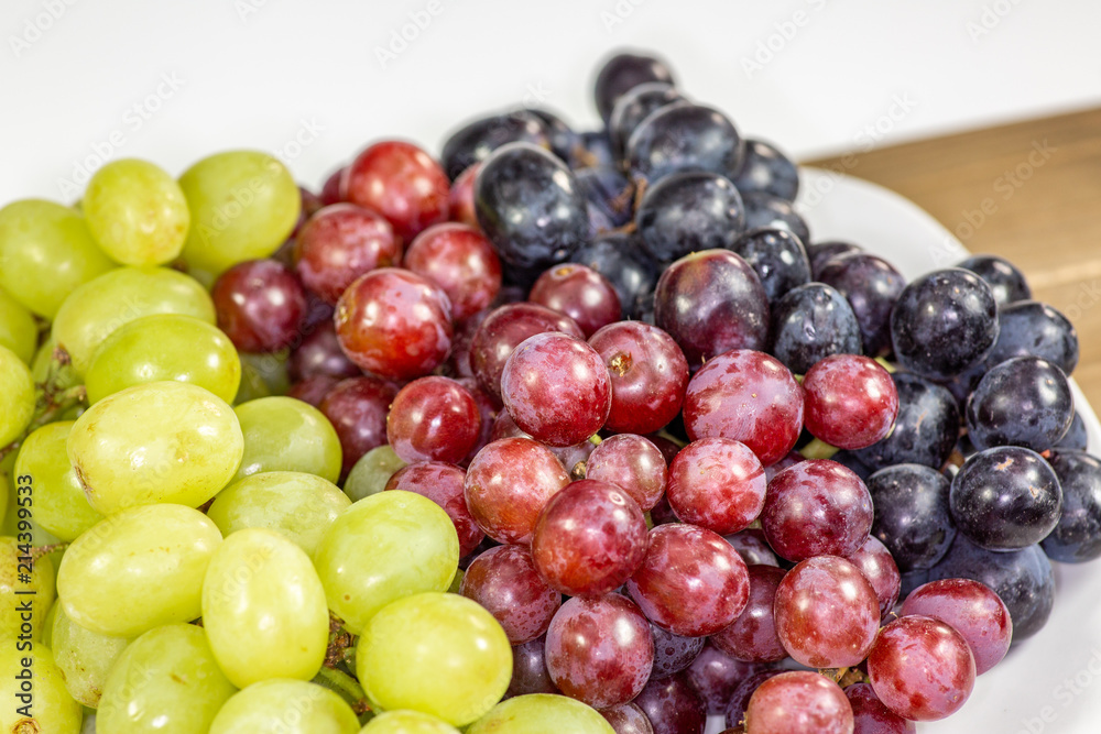Black, red, green seedless grapes in a deep white bowl on a white tale waiting to be eaten Black, red, green seedless grapes in a deep white bowl on a white tale waiting to be eaten