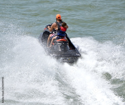 Father and his young son riding tandem running waves on a jet ski.