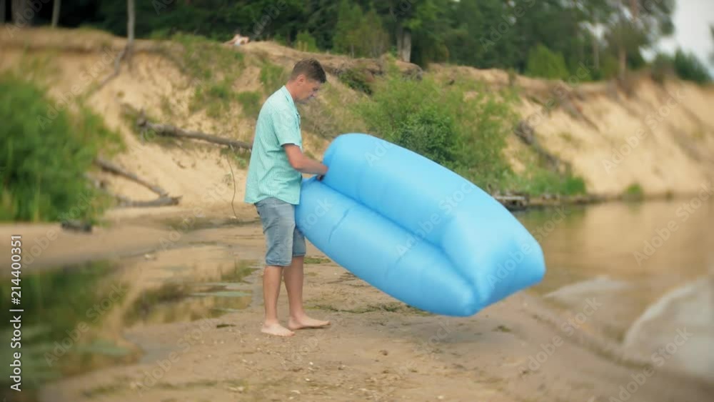 A man is inflating on an inflatable mattress by the sea. A man is inflating on an inflatable mattress by the sea.